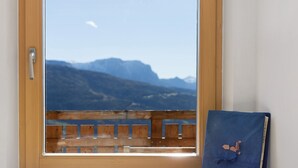 Ein Fenster mit Blick auf Berge, eine Holztür und ein blaues Buch auf einem Fensterbrett.