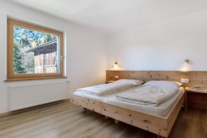 A bedroom with a wooden bed, a window with a view of trees, and a wall-mounted light.