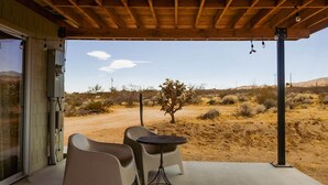 Patio esterno con due sedie e un tavolino, affacciato su un paesaggio desertico con vegetazione rada e cielo sereno.
