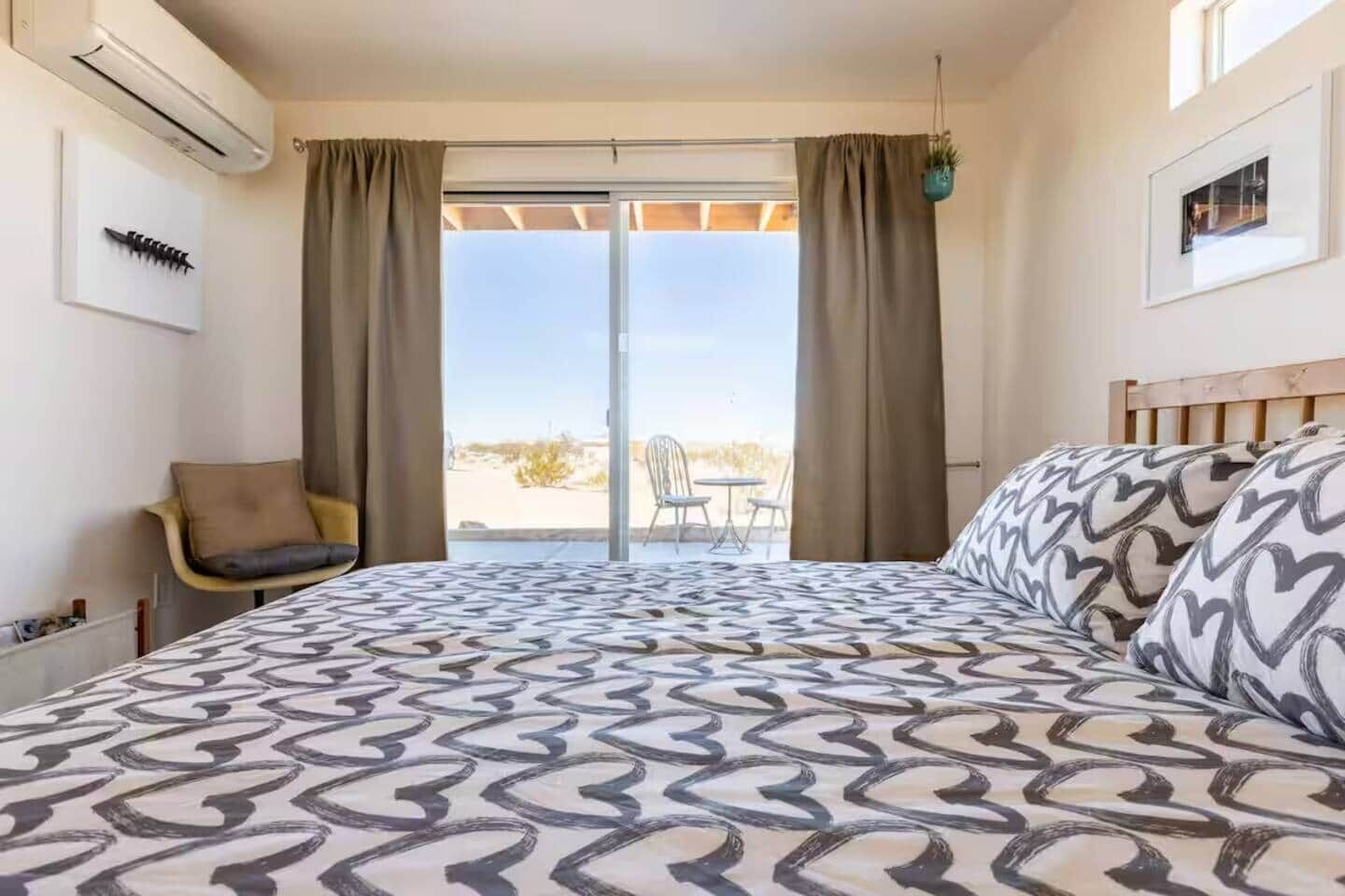 A hotel room with a bed, a chair, a window with curtains, and a view of the outdoors.