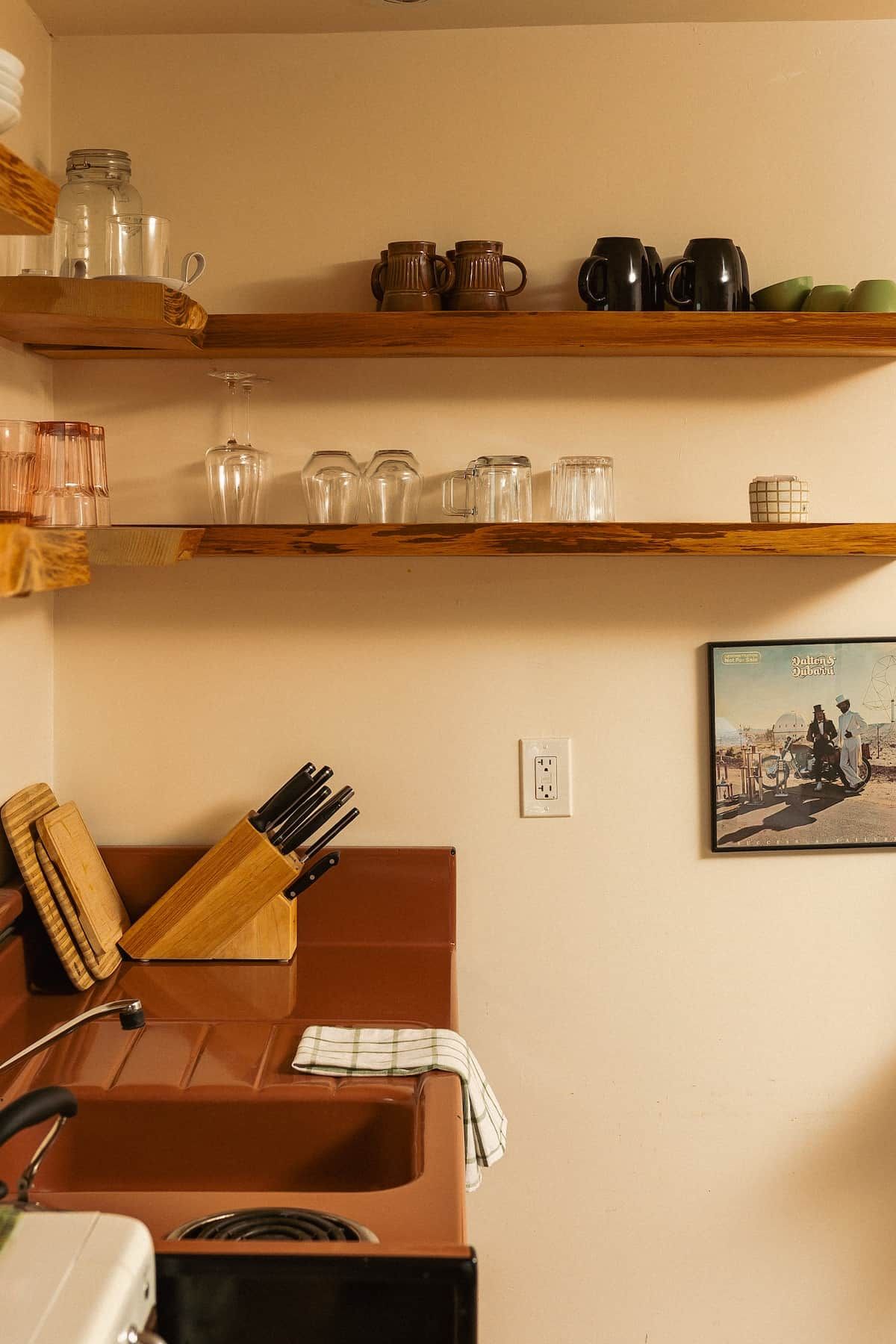 A kitchen with wooden shelves holding various glassware and a knife block.