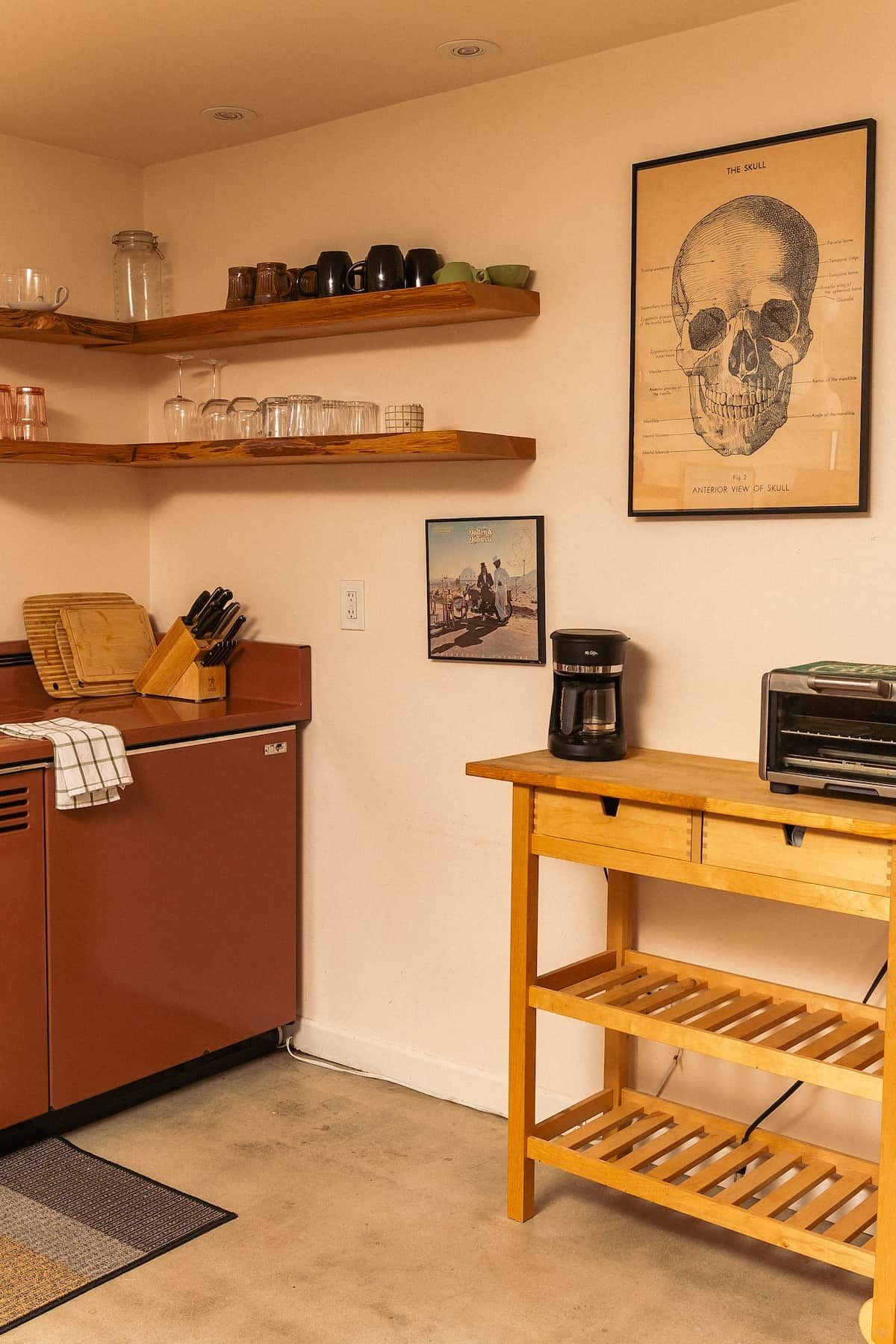 Een keuken met houten kastjes, een koffiezetapparaat en een illustratie van een schedel in een lijst aan de muur.