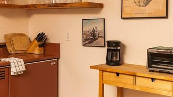 Een keuken met houten kastjes, een koffiezetapparaat en een illustratie van een schedel in een lijst aan de muur.
