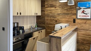A modern kitchen with wooden cabinets, a built-in oven, a coffee maker, and pendant lights.