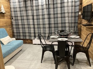 Un coin repas avec une table dressée pour quatre personnes, un canapé bleu et un rideau à carreaux.