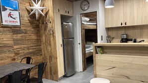 A modern kitchen with wooden cabinetry, a stainless steel refrigerator, and a small dining area with a table and chairs.