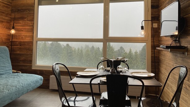 A cozy cabin-style room with a wooden interior, a dining table set for four, and a television mounted on the wall.