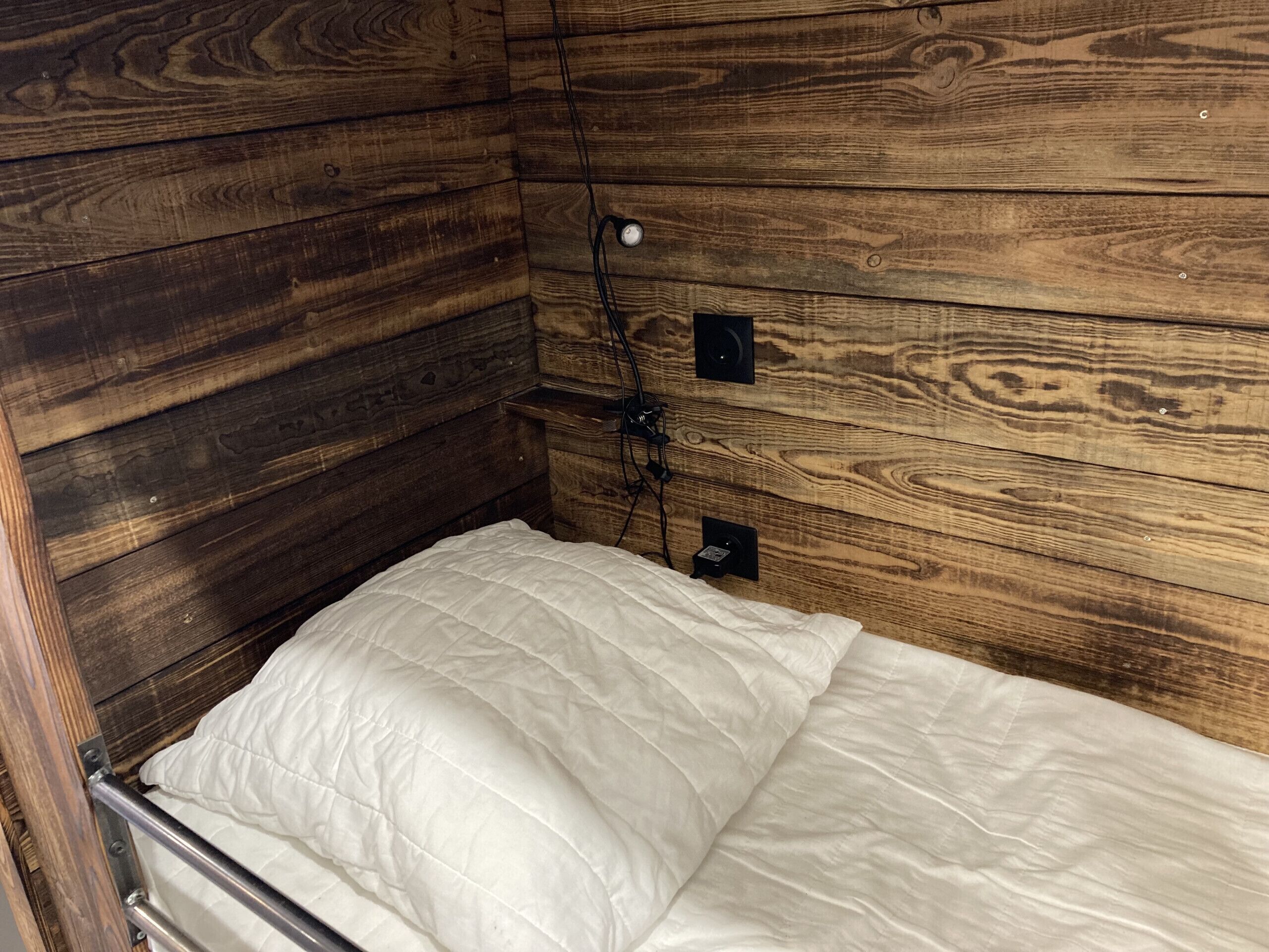 Une pièce aménagée comme un chalet en bois, avec un lit, une prise de courant et un haut-parleur fixé au mur.