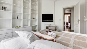 A hotel room with a large bed, a TV, a desk, and a wardrobe with multiple shelves. - NEW: Stunning spacious flat in Champs-Elysees (Paris)