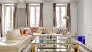 A modern living room with a glass coffee table, two sofas, and a blue ottoman. - NEW: Stunning spacious flat in Champs-Elysees (Paris)