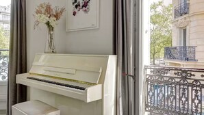A piano in a room with a balcony, a vase of flowers, and a framed artwork on the wall. - NEW: Stunning spacious flat in Champs-Elysees (Paris)