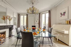 Een eetruimte met een glazen tafel, zwarte stoelen, een kroonluchter en een piano.