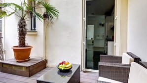 A balcony with a potted palm tree, a wicker table with a fruit bowl, and wicker furniture. - NEW: Stunning spacious flat in Champs-Elysees (Paris)