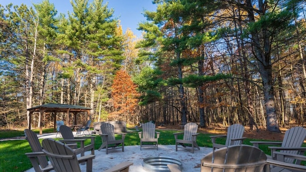 An outdoor seating area with Adirondack chairs and a fire pit, surrounded by a forested landscape. - Kavanagh Bay Resort|Hot Tub&Sauna #1 (Hayward)