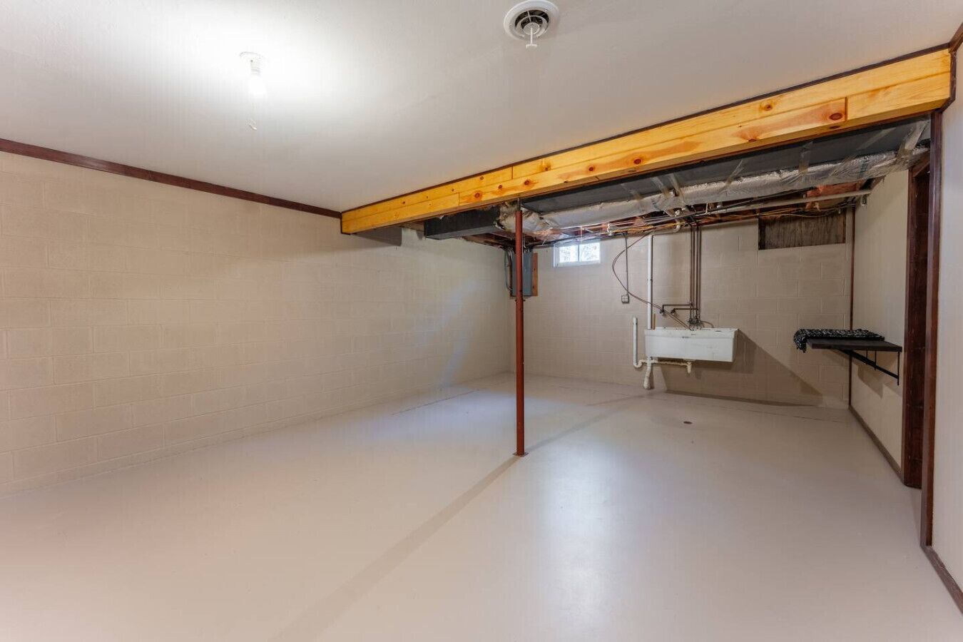 Un sótano con vigas de madera a la vista, piso de baldosas blancas y un lavamanos blanco.