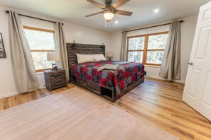 A bedroom with a wooden bed, two bedside tables, a ceiling fan, and large windows with curtains. - Kavanagh Bay Resort|Hot Tub&Sauna #1 (Hayward)