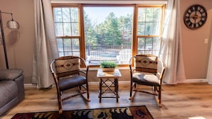 A room with two wooden chairs, a small table, and a view of trees through large windows. - Kavanagh Bay Resort|Hot Tub&Sauna #1 (Hayward)