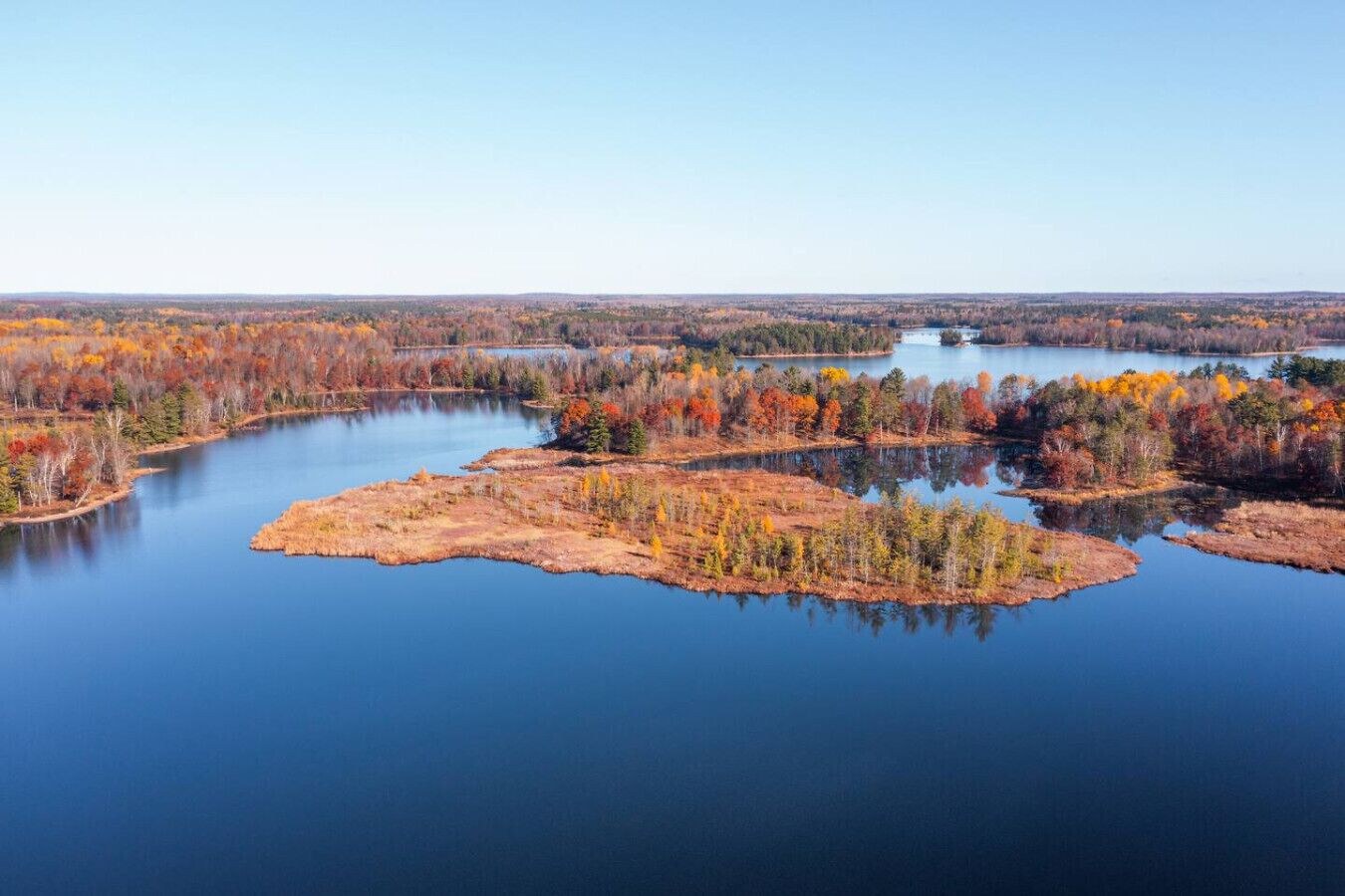 A serene lake surrounded by autumn-colored trees and a clear sky.