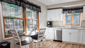A modern kitchen with white cabinets, a stainless steel dishwasher, and a dining area with a table and chairs. - Kavanagh Bay Resort|Hot Tub&Sauna #1 (Hayward)
