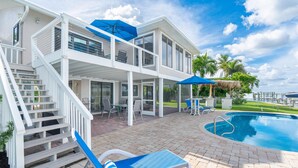 Una casa moderna con piscina, mobiliario exterior y una escalera que lleva a un balcón.