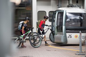 Zwei Radfahrer mit Fahrrädern in der Nähe einer Straßenbahn, was auf ein öffentliches Verkehrssystem hinweist.
