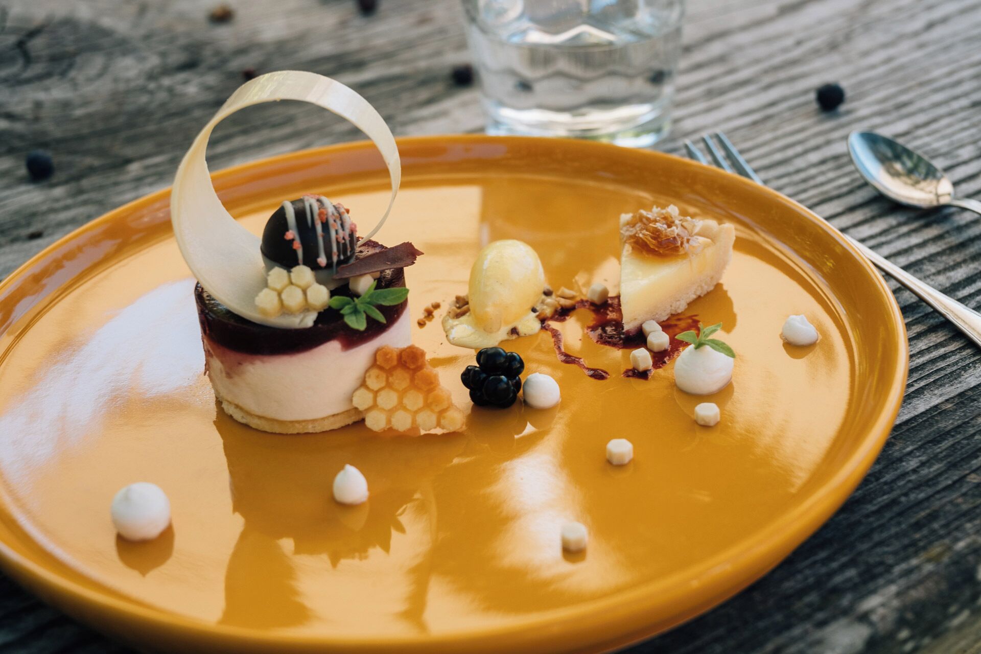 A dessert plate with a variety of sweets and a glass of water on a wooden table.
