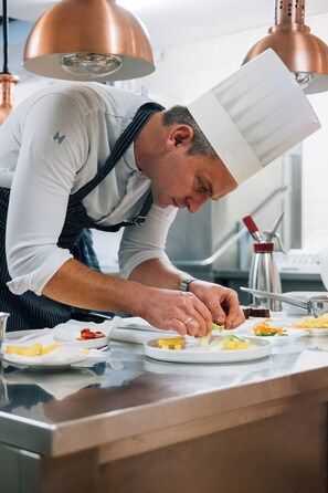 A chef preparing food in a kitchen with copper lighting fixtures and stainless steel appliances. - APIPURA hotel rinner (Renon)