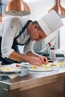 Un chef preparando comida en una cocina con lámparas de cobre y electrodomésticos de acero inoxidable.