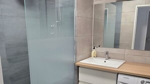 Et moderne badeværelse med en glasbrusekabine, en vask med spejl og en vaskemaskine.