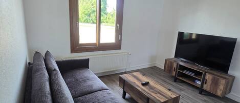 Una sala moderna con un sofá modular, una mesa de centro de madera, un mueble para televisión y un ventanal con vistas a zonas verdes.