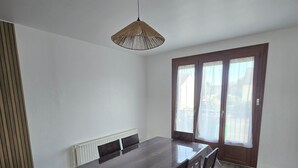 Et spiseområde med et træbord og stole, en hængende lampe samt udsigt gennem en glasdør.