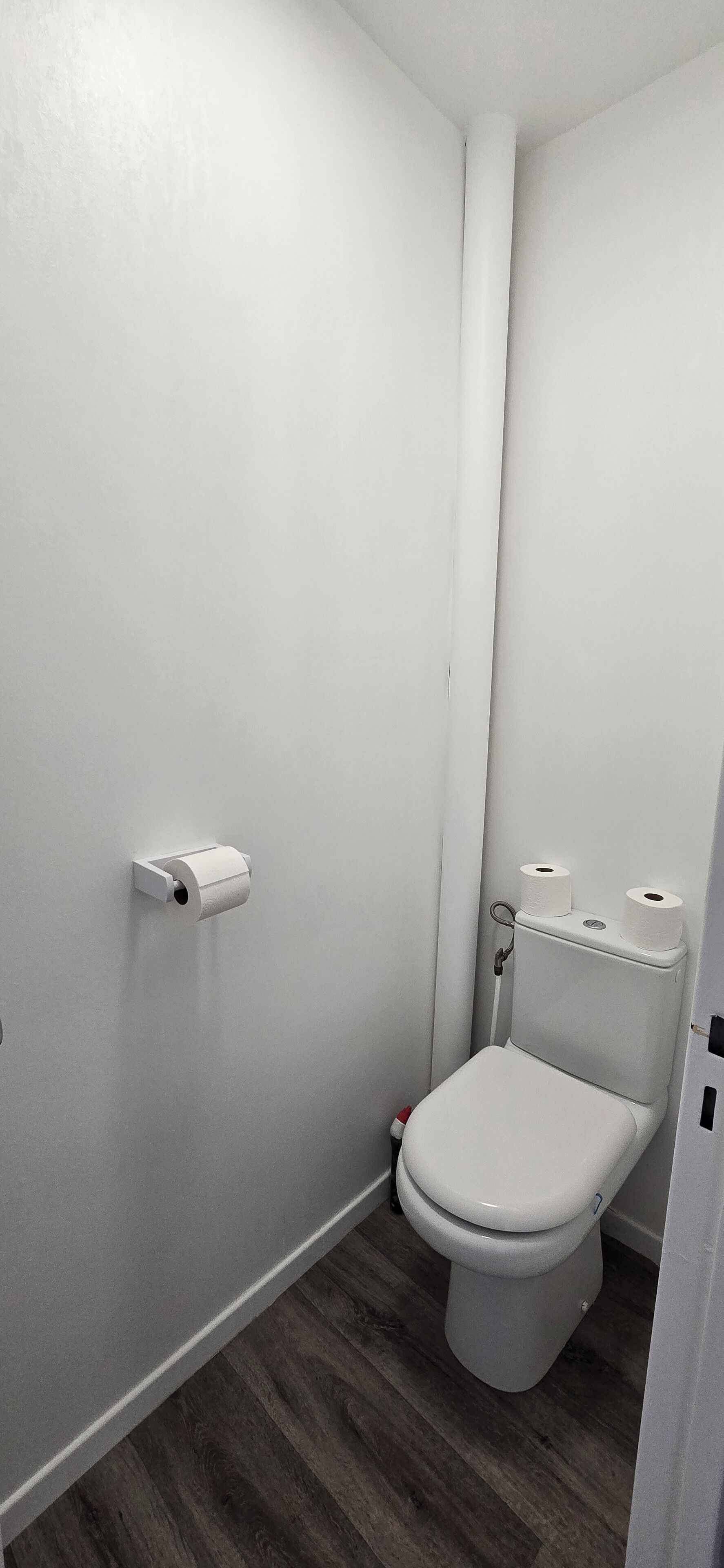 A small, white bathroom with a toilet, a toilet paper holder, and a wooden floor.