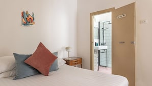 Ein Schlafzimmer mit Bett, Kissen, einem Nachttisch mit Lampe und einer Tür zu einem Badezimmer mit Dusche.