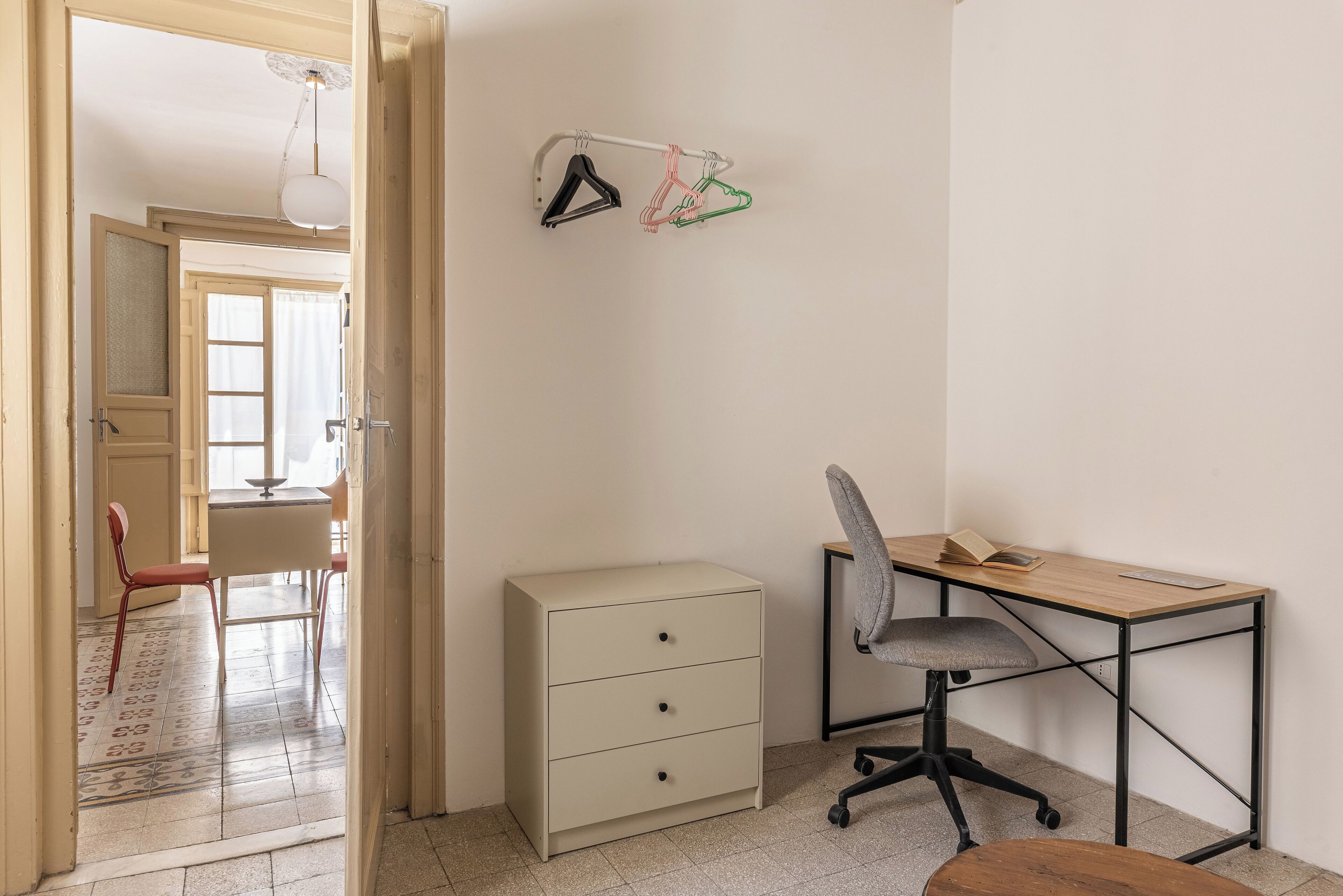 Ein Zimmer mit Schreibtisch, Stuhl und Schrank. Eine Tür führt in einen anderen Raum.