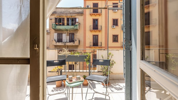 Ein Balkon mit zwei Stühlen und einem kleinen Tisch, mit Blick auf eine Reihe von Gebäuden mit Balkonen und Klimaanlagen.