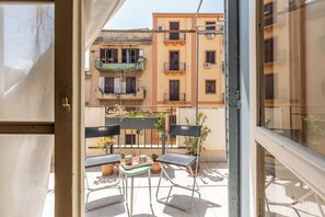 En balkon med to stole og et lille bord, med udsigt over en række bygninger med både balkoner og ventilationsanlæg.