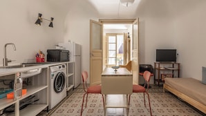 Ein kleines Zimmer mit Waschmaschine, Spüle, einem kleinen Tisch mit Stühlen, einem Bett und einem Fernseher.