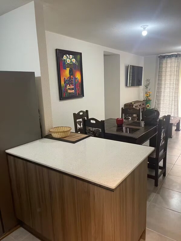 A compact kitchen with a central island, wooden cabinets, and a dining area with chairs and a TV mounted on the wall.