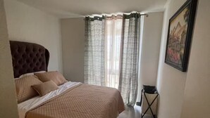 A bedroom with a bed, curtains, a painting, and a small table.