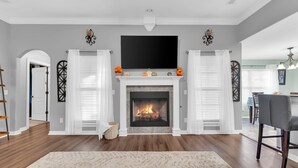 Una sala de estar con chimenea, un televisor de pantalla plana en la parte superior y un comedor al fondo.