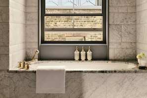 A bathroom with a marble sink, gold fixtures, and a view of a brick wall through a window. - Cambridge House, Auberge Collection (London)