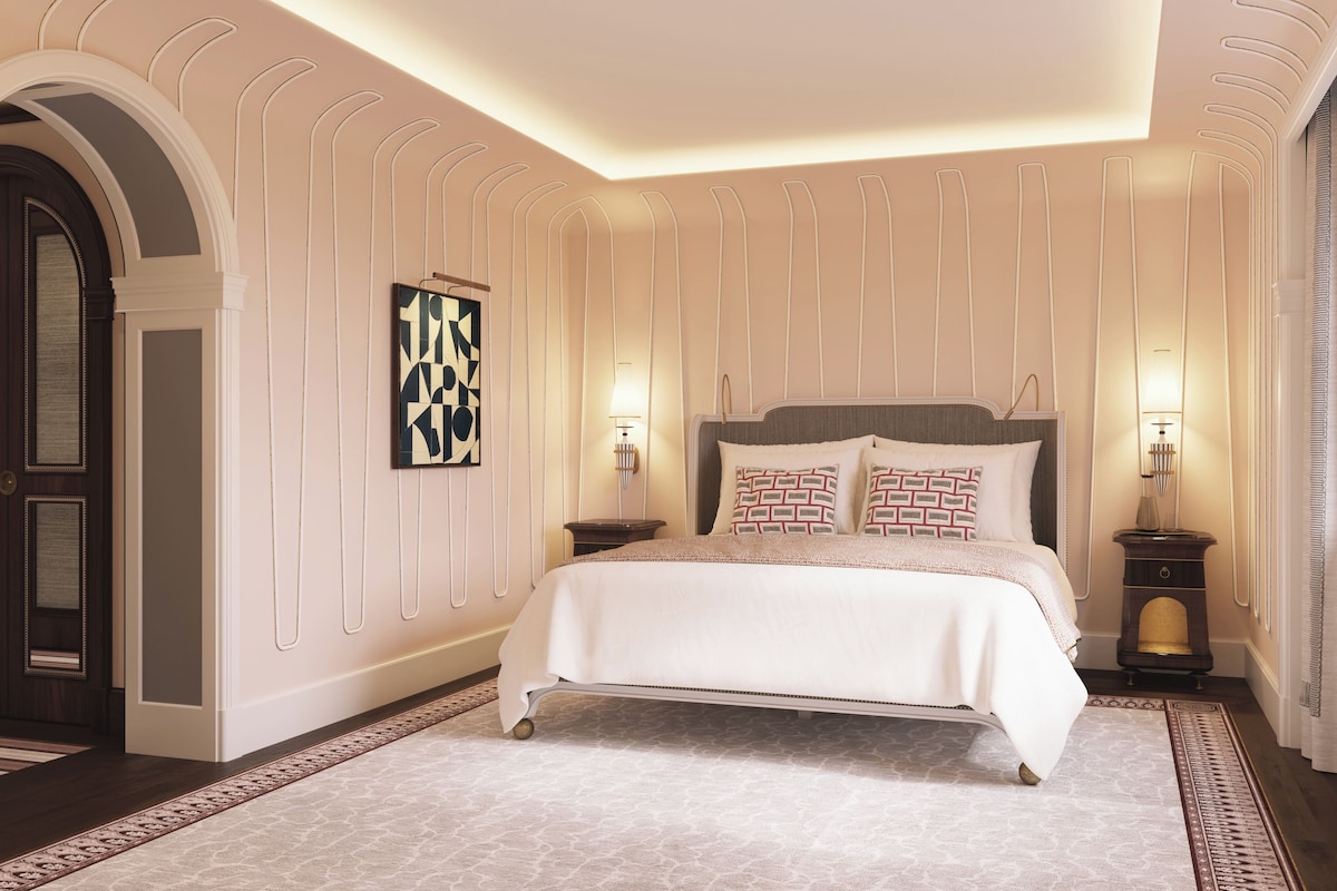 A bedroom with a large bed, a nightstand, a wall-mounted lamp, and a decorative wall panel.