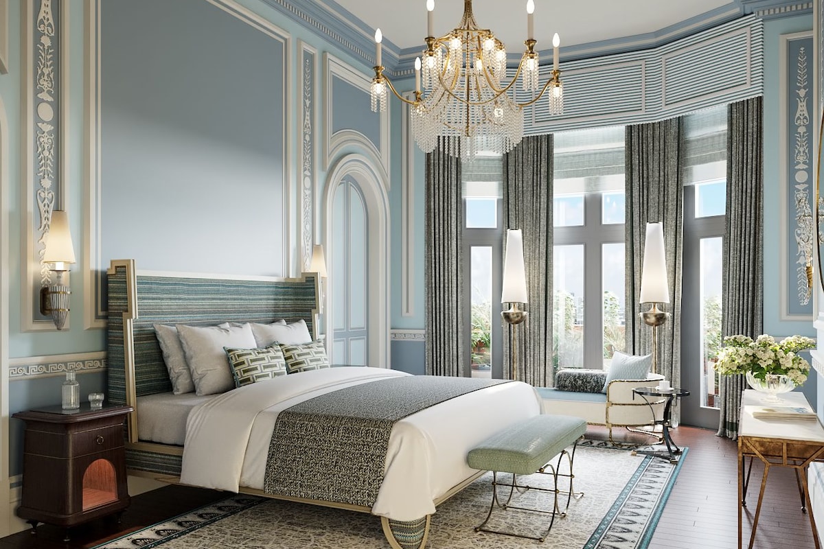 A spacious bedroom with a large bed, a chandelier, and a view of the city through large windows.