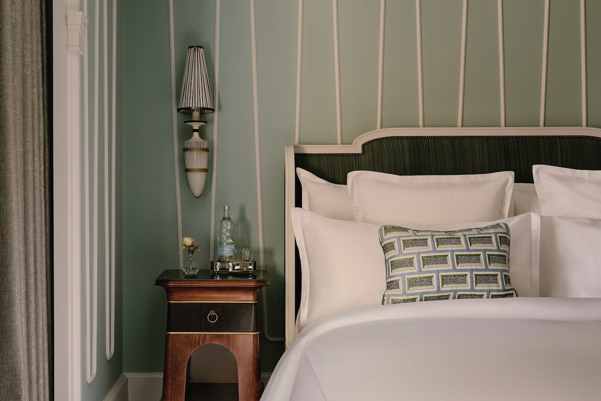 A hotel room with a bed, a nightstand, a lamp, and a window with curtains.