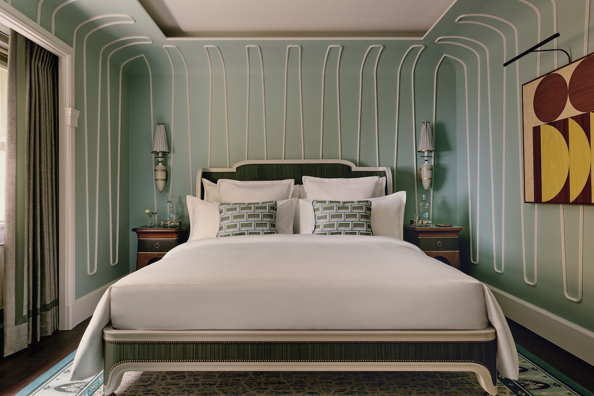 A large bed with white linens, a headboard with a green upholstered panel, and two bedside tables with lamps.