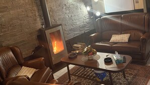 A cozy living room with a fireplace, leather sofas, a coffee table with snacks, and a modern pendant light. - Vacation Home in Tubize (TUBIZE)