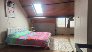A bedroom with a bed, a skylight, a window, and a wooden ceiling.