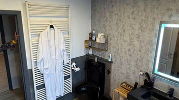 Un baño con piso de madera, una bata blanca colgada en un perchero, una bañera negra, un espejo y un lavamanos.