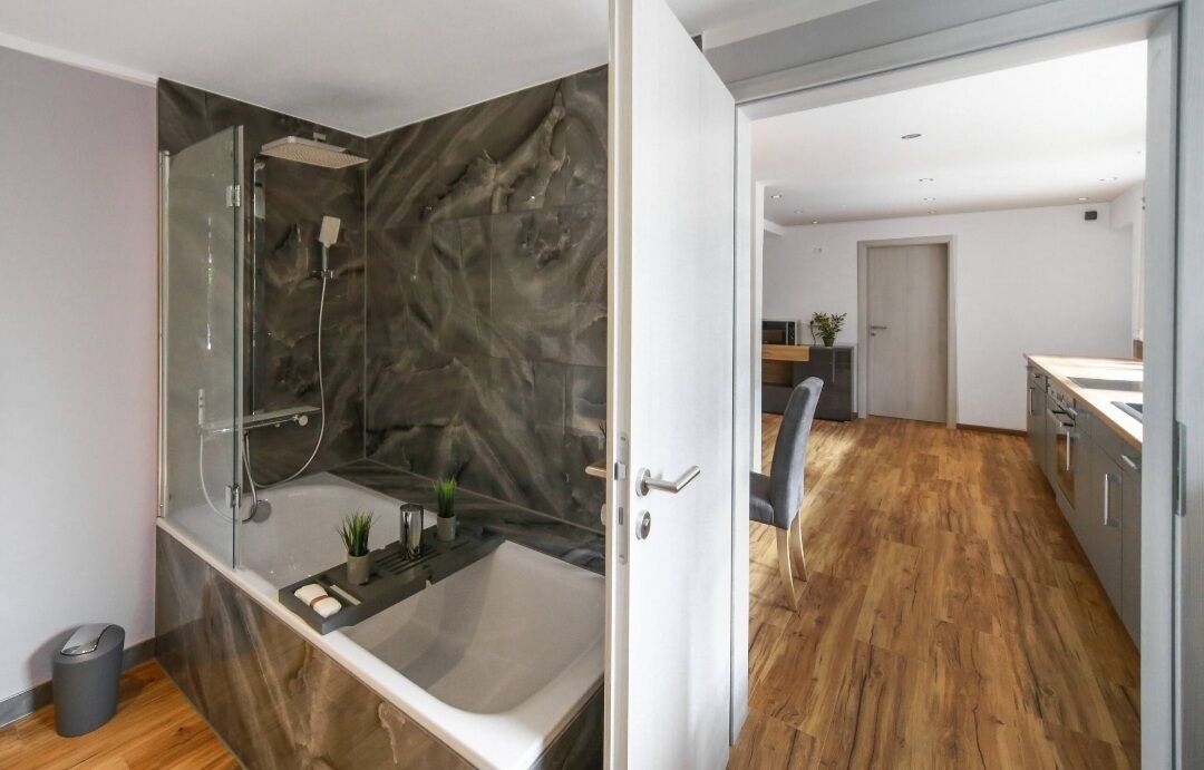 A modern bathroom with a glass-enclosed shower, a freestanding bathtub, and a marble wall.