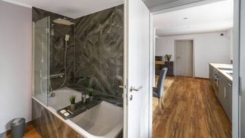 A modern bathroom with a glass-enclosed shower, a freestanding bathtub, and a marble wall.